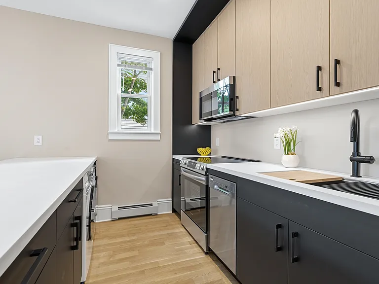 Contemporary kitchen featuring two-tone cabinetry, stainless steel appliances, white countertops, chef's sink, and light wood-finish floorin