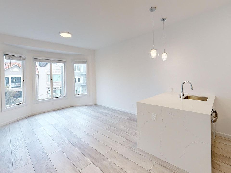 Living room with a window, wood-like flooring, and entrance to the kitchen