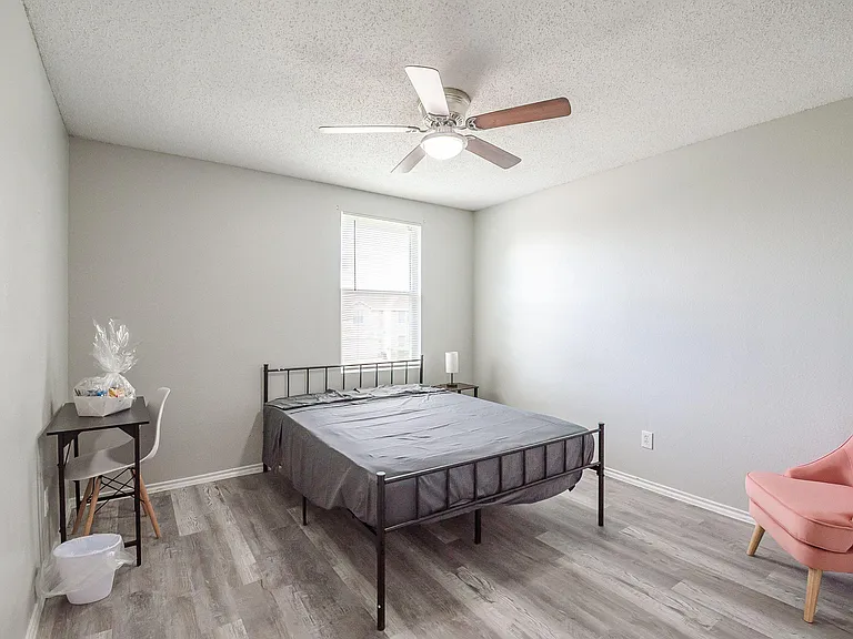 Furnished bedroom with bed, desk setup, and ceiling fan, plus a window for natural light and easy-care flooring.