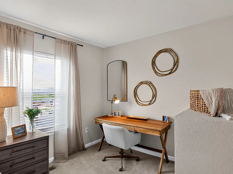 Bright and cozy home office featuring a sleek wooden desk, stylish decor, and a large window with sheer curtains.