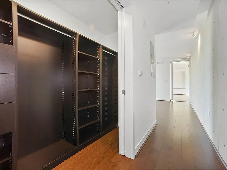 This well-designed walk-in closet offers ample storage with customizable shelving and drawers, seamlessly connected to a light-filled hallway.