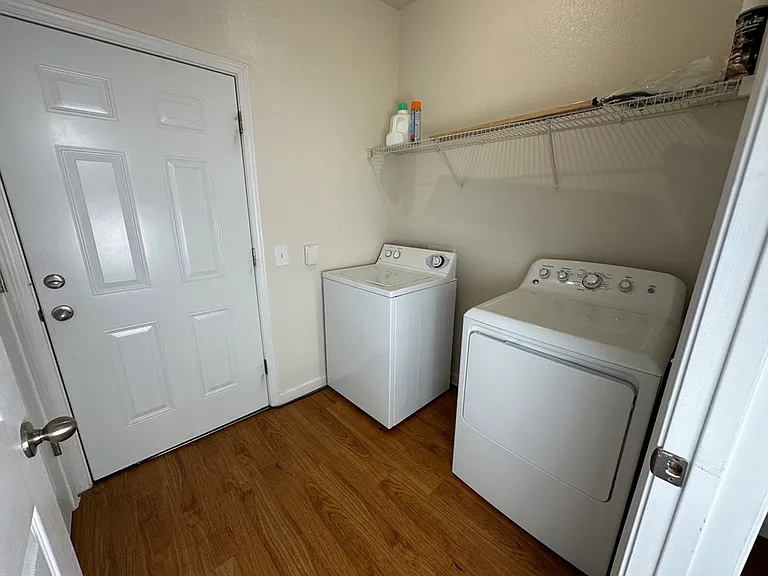 Bright laundry room with modern washer and dryer, featuring wood-look flooring and ample shelving space. Bright laundry room with modern washer and dryer, featuring wood-look flooring and ample shelving space.