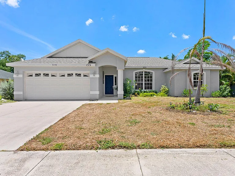 Single-story home with a covered entry, wide driveway, two-car garage, and front landscaping with mature palms.
