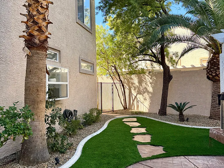 Thoughtfully landscaped backyard featuring mature trees, artificial turf, and a stepping-stone path to the gated pool