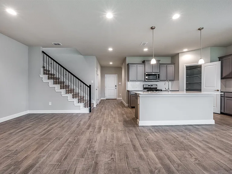 Kitchen with decorative light fixtures, wood-type flooring, a center island with sink, and stainless steel appliances