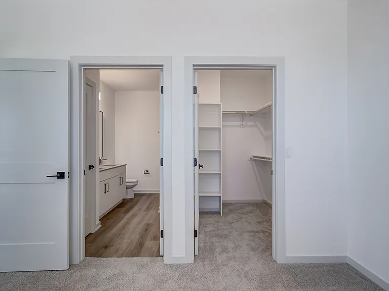 Two side-by-side doors reveal everything you'd expect from a primary suite _ a private bathroom and a walk-in closet with custom shelving.