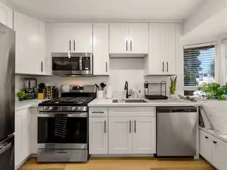 Modern kitchen with white cabinetry, stainless steel appliances, and stone benchtops, featuring a coffee machine, blender, stove cooktop, and plenty of natural light.