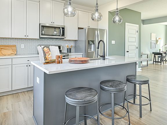 DRB Homes Whitaker II Model - Open kitchen with white cabinets, gray island with sink, white counter