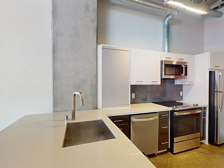 Apartment kitchen with stainless steel appliances, quartz countertops and wood-style flooring.