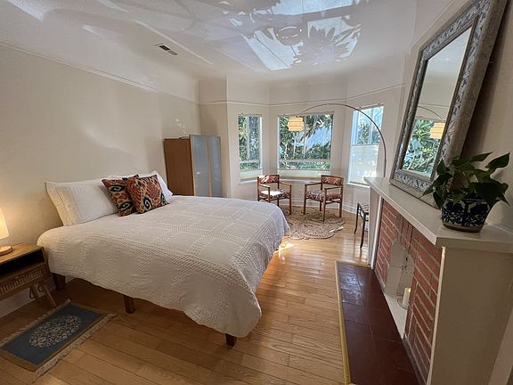 Front right bedroom with bay window, armoir, queen bed, lamp, built in shelving, mirror.