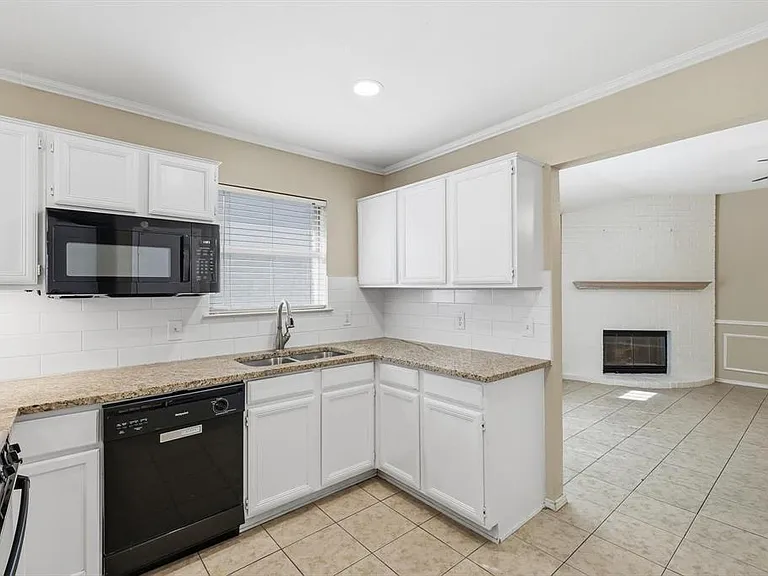 Kitchen with black appliances, crown molding, a fireplace, white cabinets, and light stone countertops