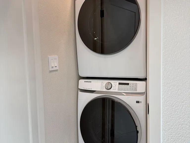 Hallway closet with stacked washer and dryer plus shelving space.