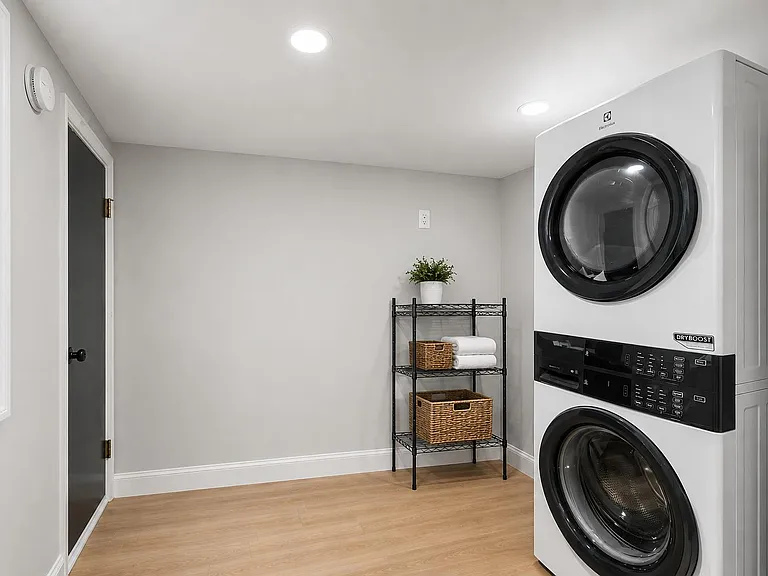 Dedicated laundry area with stacked front-load washer/dryer, open shelving for linens, and easy-care flooring.