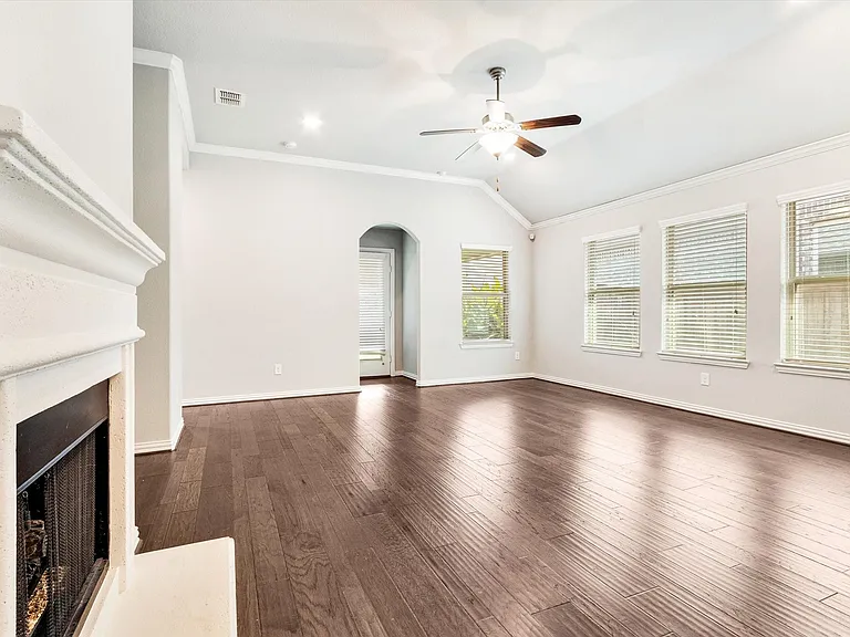 Spacious interior featuring dark wood-finish flooring, a white mantel fireplace, and vaulted ceilings with a ceiling fan