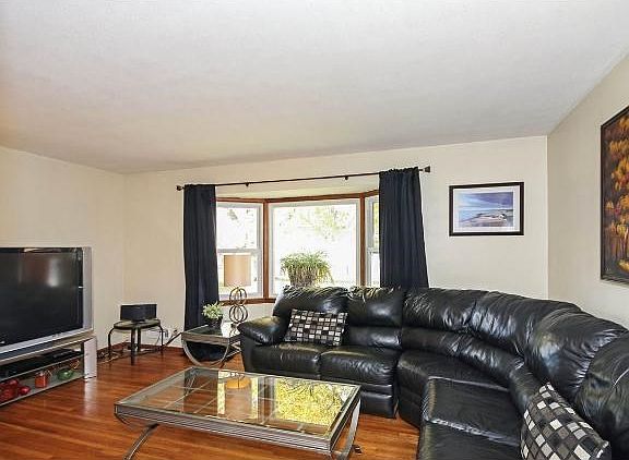 Living room with hardwood floors and large bay window that overlooks the backyard.