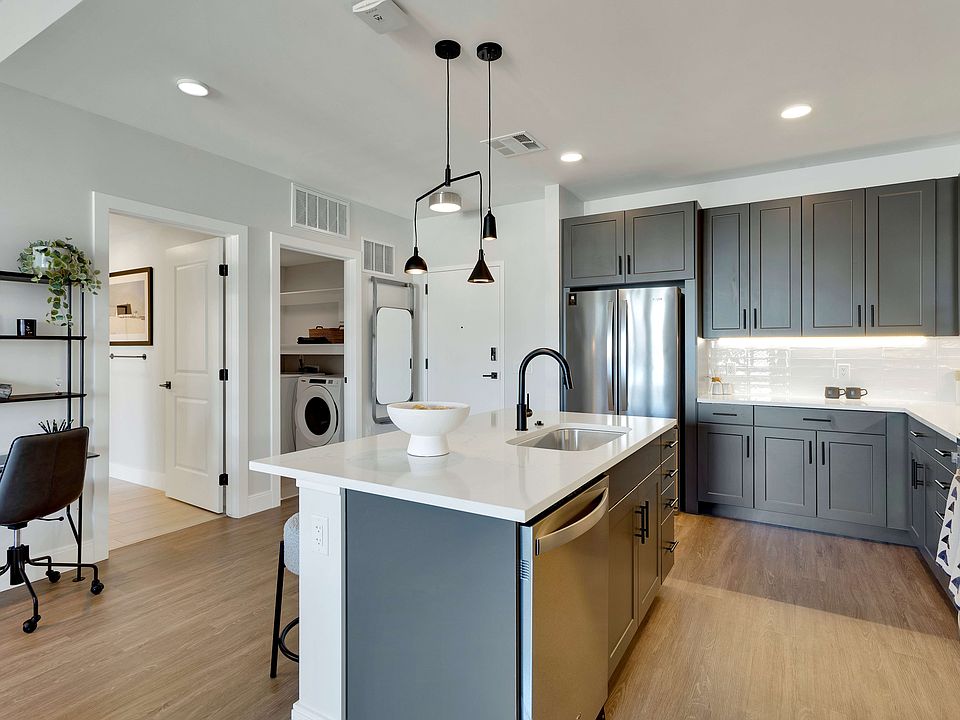 Modern kitchen with sleek dark cabinets, elegant pendant lighting, and a spacious island with integrated sink, offering a stylish workspace.