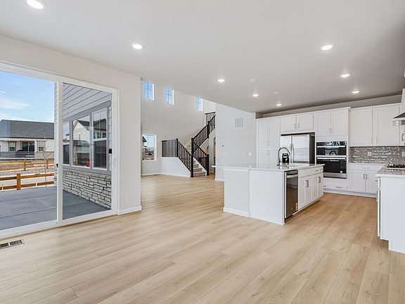 A spacious and modern kitchen with white cabinets, stainless steel appliances, and hardwood floors,