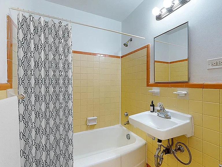 Charming bathroom featuring vintage yellow tiles, a sleek porcelain sink, and a classic bathtub with a pattern shower curtain.