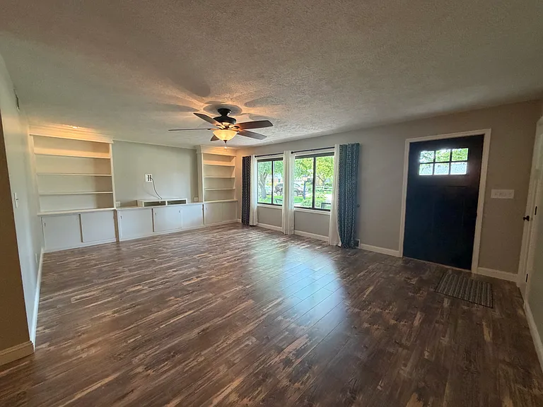 Large open living room with picture window and built-in shelving and storage cabinets. Coat closet at front door.