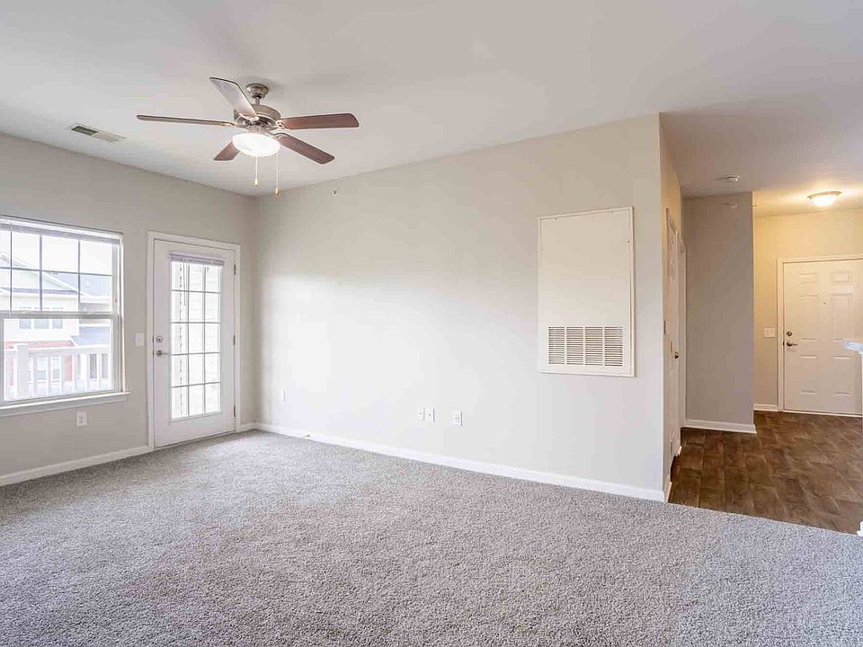 Open living area with ceiling fan, plush carpet, and view into hallway and entry, providing functional flow at Cedar Terrace Apartments.