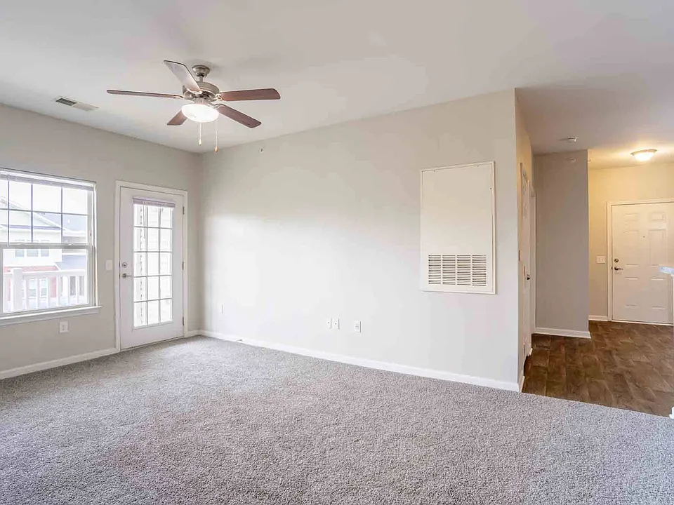 Open living area with ceiling fan, plush carpet, and view into hallway and entry, providing functional flow at Cedar Terrace Apartments.