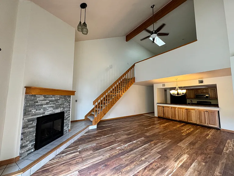 View from the loft overlooking the vaulted main living area, fireplace, private deck, and surrounding trees _ a rare top-floor Genesee Village layout.