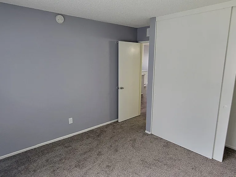 Carpeted bedroom with large window and closet at Grand Oaks Apartments in Lake Elsinore, California.