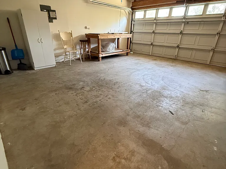 Garage with workbench and small cabinet. Additional ceiling shelving on the opposite wall.