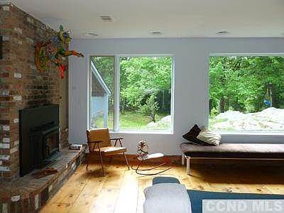 Living room, fireplace, and views through large windows to a rocky outcrop, open spaces, and mature trees leading to the lake.