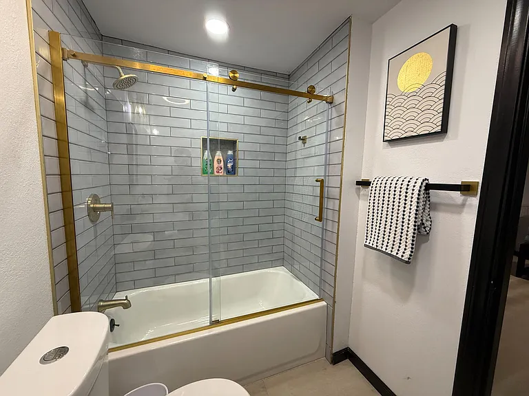 Updated tub/shower combo with subway tile surround, glass sliding doors, and built-in niche shelving.