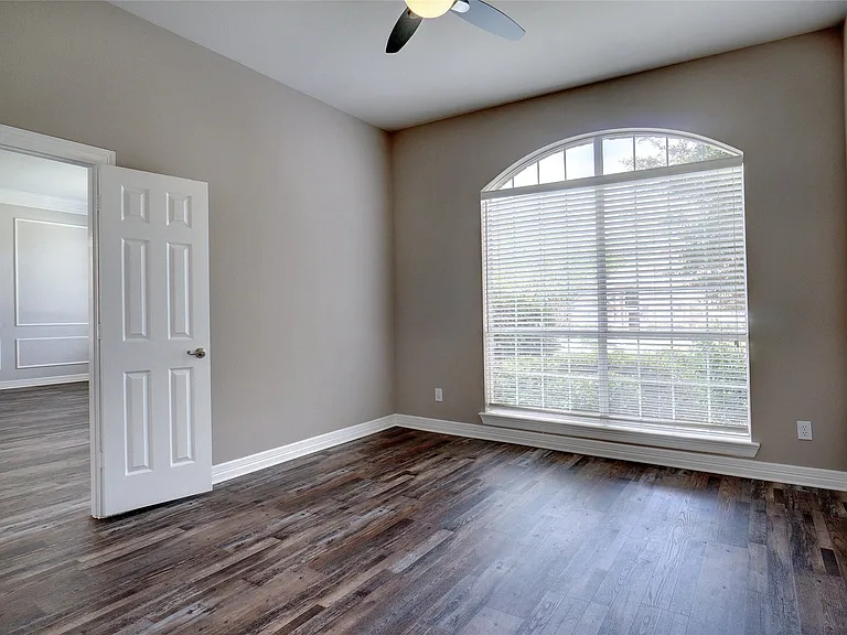 Room featuring an arched window with horizontal blinds, wood-finish flooring, neutral wall paint, and white baseboards
