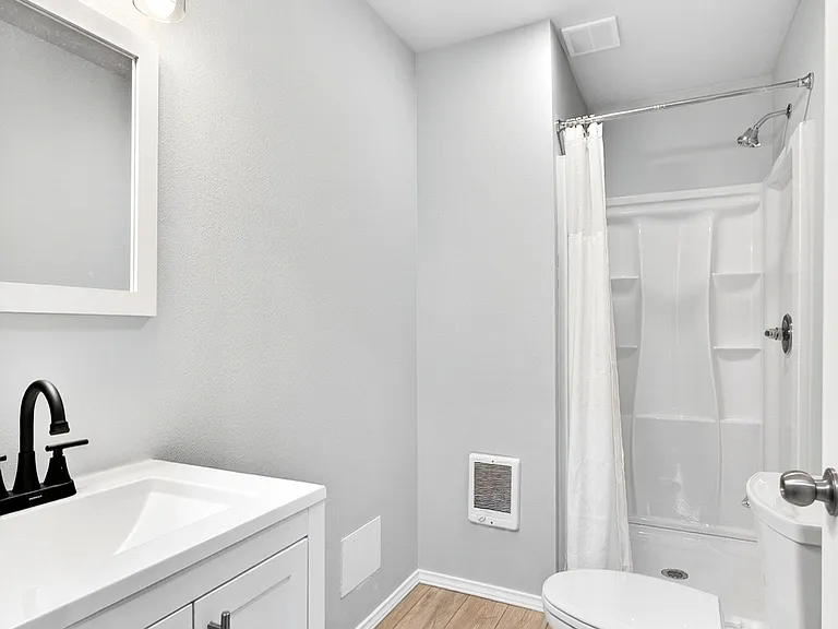 Efficient full bath with a single-sink vanity, framed mirror, and tub/shower combo with built-in shelving.