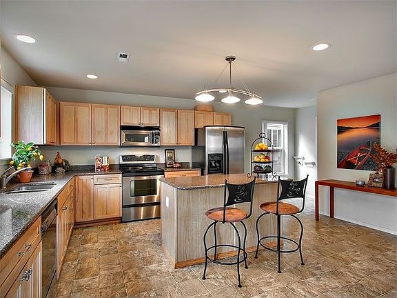 Kitchen w/ stainless, engineered stone counters & maple cabinets.