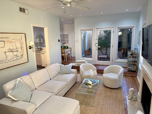 The living room has a gas fireplace. There is a breakfast bar and dining area at the back right, and french doors open to a private outdoor patio.