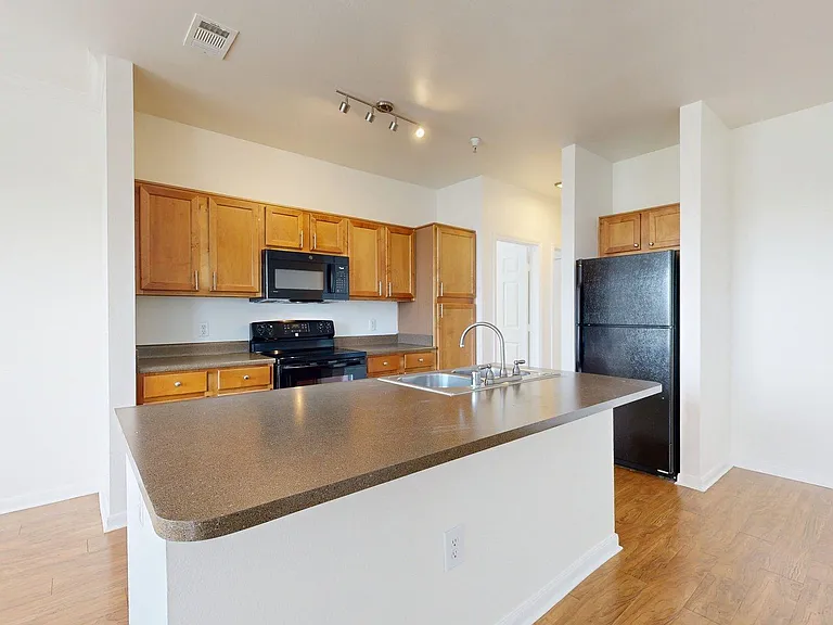 Apartment kitchen with black appliances, dark countertops, and wood style floors.