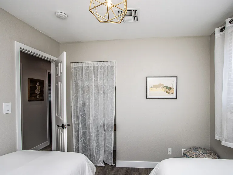 Charming twin bedroom at Casa Del Sol, Tempe rental home. Features two twin beds with unique geometric headboards, gold pendant lighting, "Relax and Unwind" wall art, and a patterned pouf. Ideal for family or group stays in Tempe, AZ.