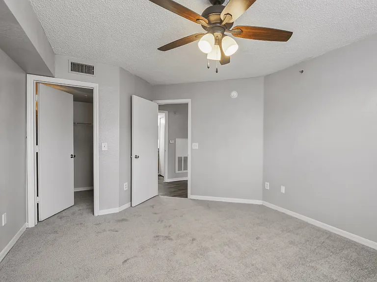 Bedroom with plush carpeting, ceiling fan, walk-in closet entrance, and doorway leading to the living area in a 1-bedroom apartment at Gregory Cove in Jacksonville, FL.