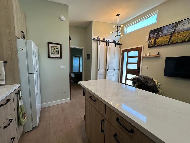kitchen island, view looking towards Bedroom #1. White barn-style doors to the left of front door have storage/coat closet behind them.