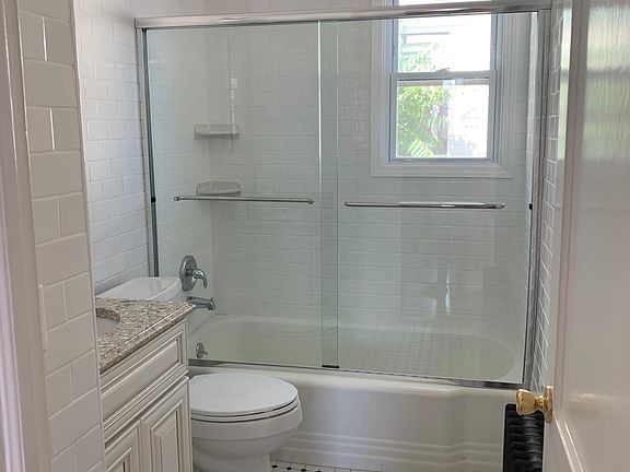Bathroom with brand new shower doors, floor to ceiling white subway tiles, new combo fan/LED lighting, new vanity with stone top and backsplash.