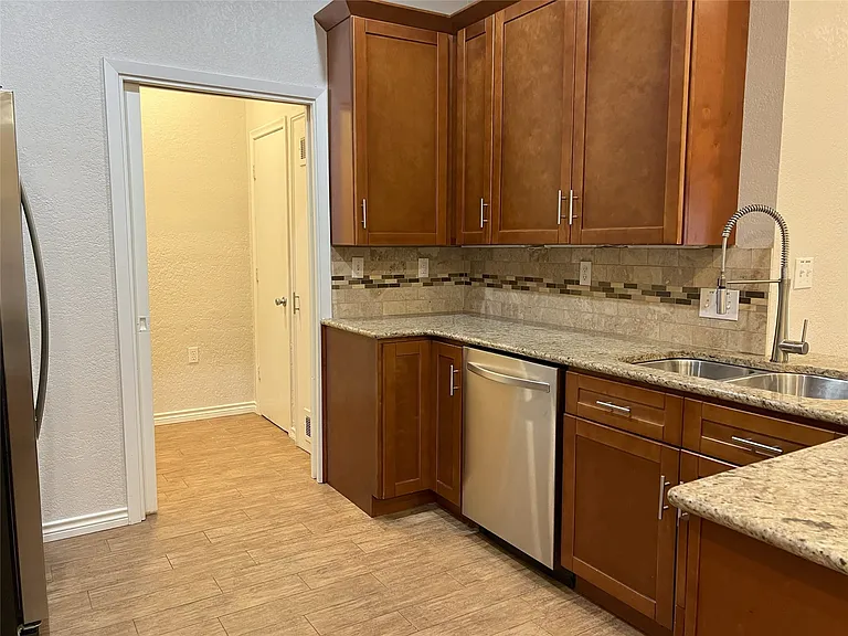 Kitchen featuring wood-finish cabinetry, granite-style countertops, stainless steel appliances, a double basin sink with a high-arc faucet, and tiled flooring. Utility room accommodates a full sized washer and dryer and also has pantry storage.