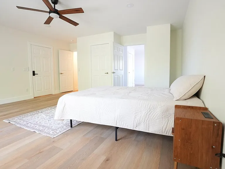 Spacious bedroom with a ceiling fan, wide-plank flooring, and room for a full/queen bed plus additional furniture.