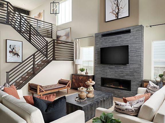 A modern and cozy living room with a fireplace, a TV, and a wooden staircase leading to an upper lev