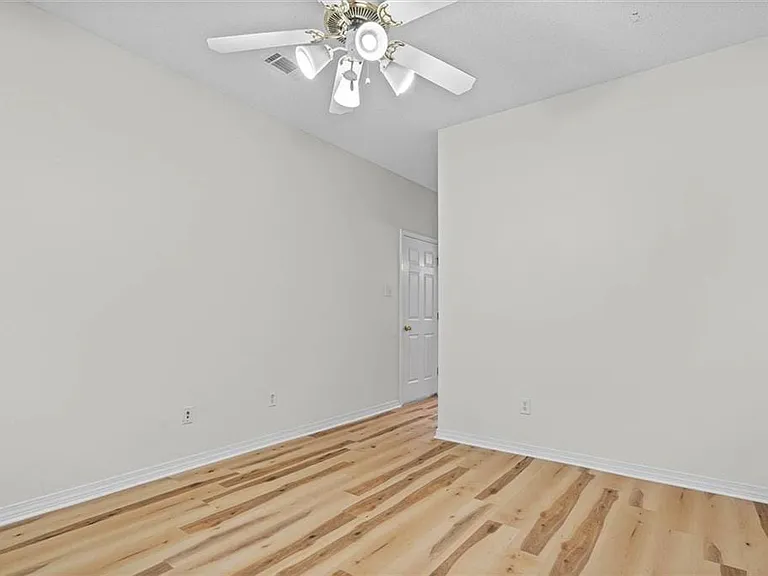 Spacious room featuring wood-finish flooring, light-toned walls, and a ceiling fan with integrated lighting