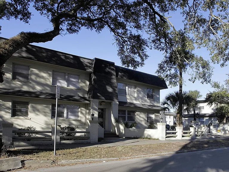 Charming two-story apartment building surrounded by lush trees, offering a serene suburban feel and ample natural light.