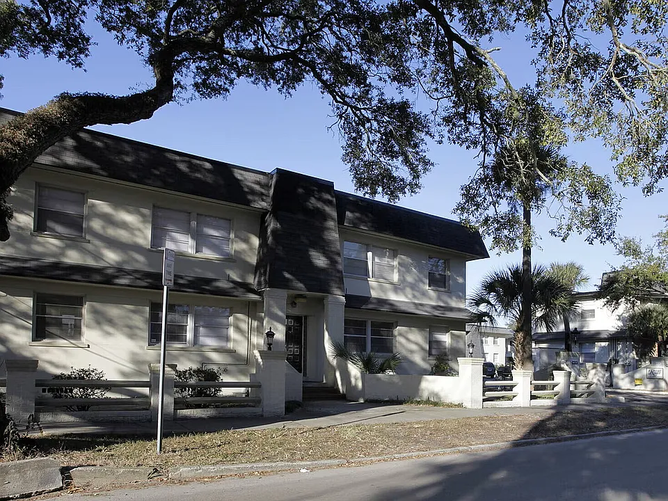 Charming two-story apartment building surrounded by lush trees, offering a serene suburban feel and ample natural light.