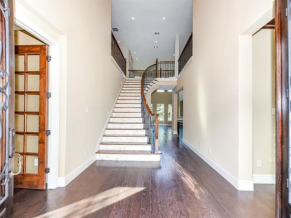 Grand entrance with wood flooring, double wrought iron and wood front doors, wood and stone staircase