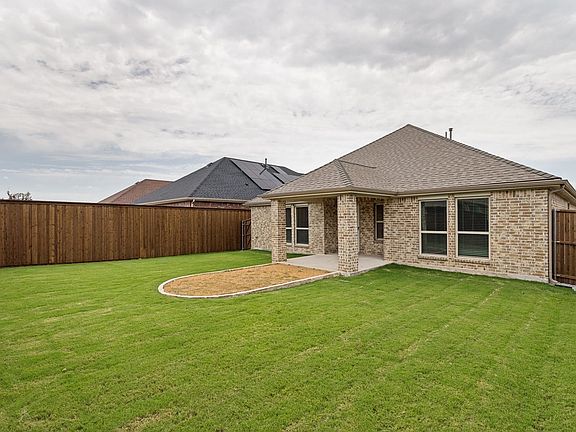 Expansive backyard featuring a manicured lawn, a covered patio with brick columns, and a defined planting area