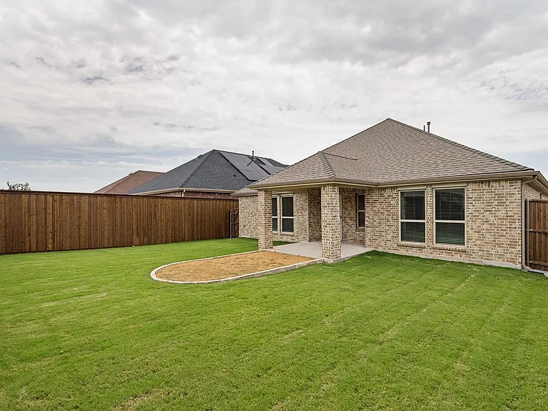 Expansive backyard featuring a manicured lawn, a covered patio with brick columns, and a defined planting area