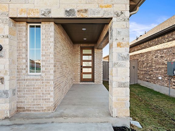 A covered walkway leading to a modern brick and stone house, with a grassy yard visible in the backg