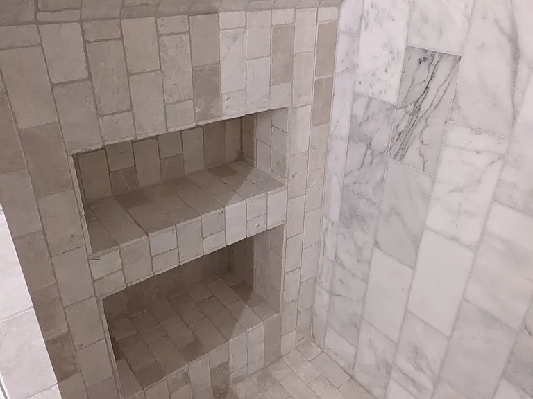 Generously sized marble tile shower with built-in storage nook